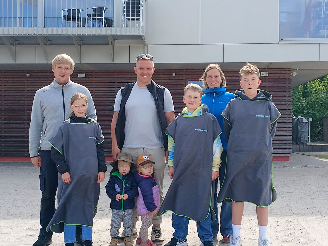 Unternehmer Max Bornhöft von Baumdienst Nord übergibt vor dem DLRG-Gebäude in Stralsund den Kindern der DLRG-Jugend neue Ponchos.